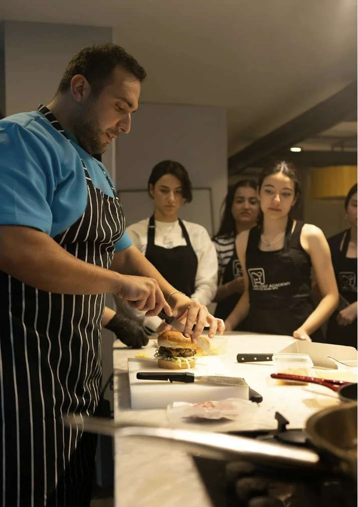 Chef cuisinier coupe un burger gourmet devant des participants lors d’un atelier cuisine à Lyon
