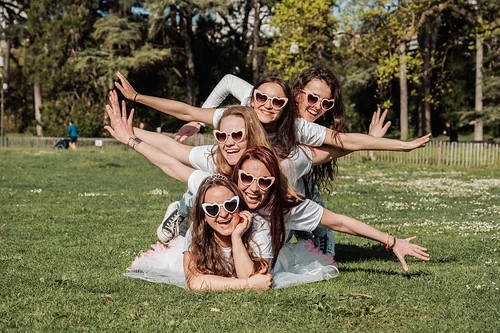 Cinq femmes souriantes avec lunettes en forme de cœur formant une pyramide humaine sur l’herbe lors d’un city game spécial EVJF