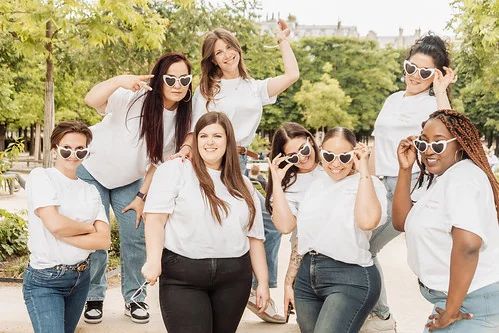 Groupe d’amies en t-shirts blancs et lunettes cœur posant ensemble lors d’un clip vidéo EVJF à Paris