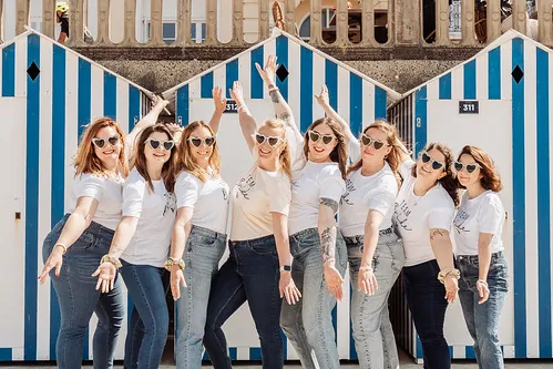 groupe de femmes en tenue coordonnee pose joyeusement devant des cabines de plage bleues et blanches à cabourg