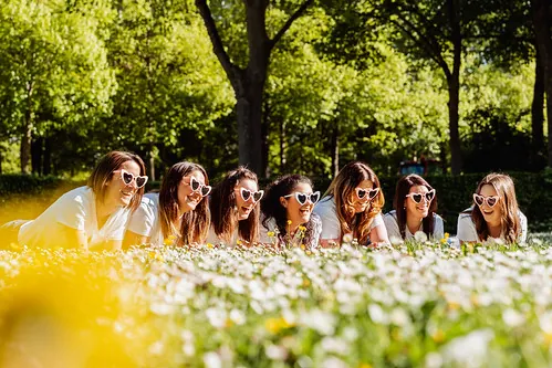 groupe de femmes allongees dans l herbe avec des lunettes coeur souriant dans un parc fleuri à cabourg