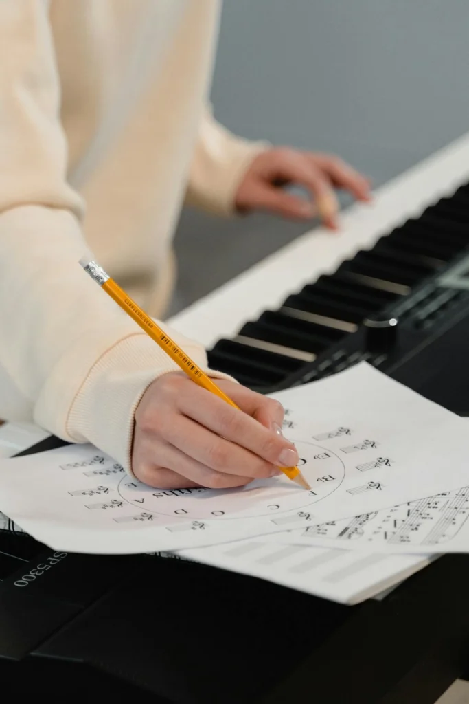 Personne écrivant de la musique sur une feuille à côté d’un clavier numérique.