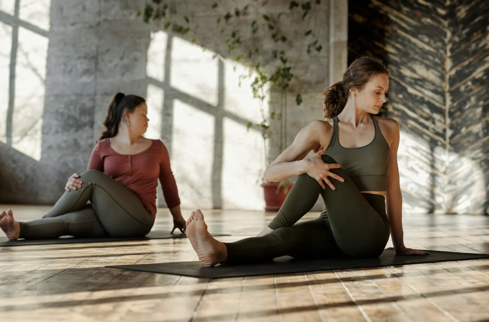 Deux femmes réalisant une torsion assise lors d’un cours de yoga dans une salle ensoleillée à Bordeaux