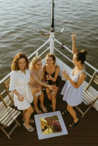 Quatre amies profitant d'un aperitif sur le pont d'un bateau a Bordeaux, verres de vin rose et plateau de fromages et fruits.