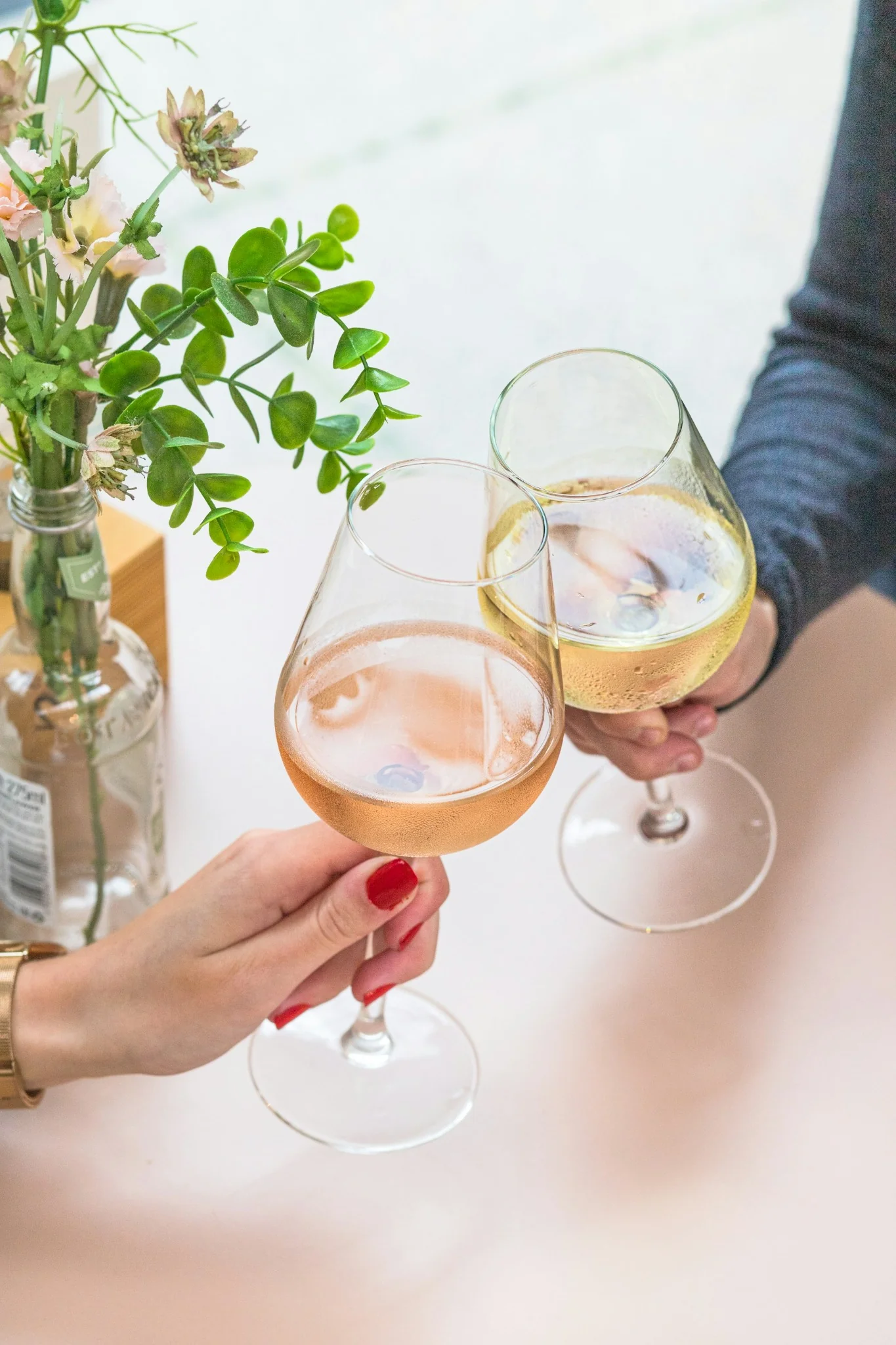 Deux personnes trinquant avec un verre de vin rosé et un verre de vin blanc sur une table fleurie