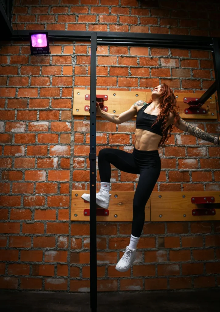 Femme en tenue de sport noire grimpant sur une structure devant un mur en briques.