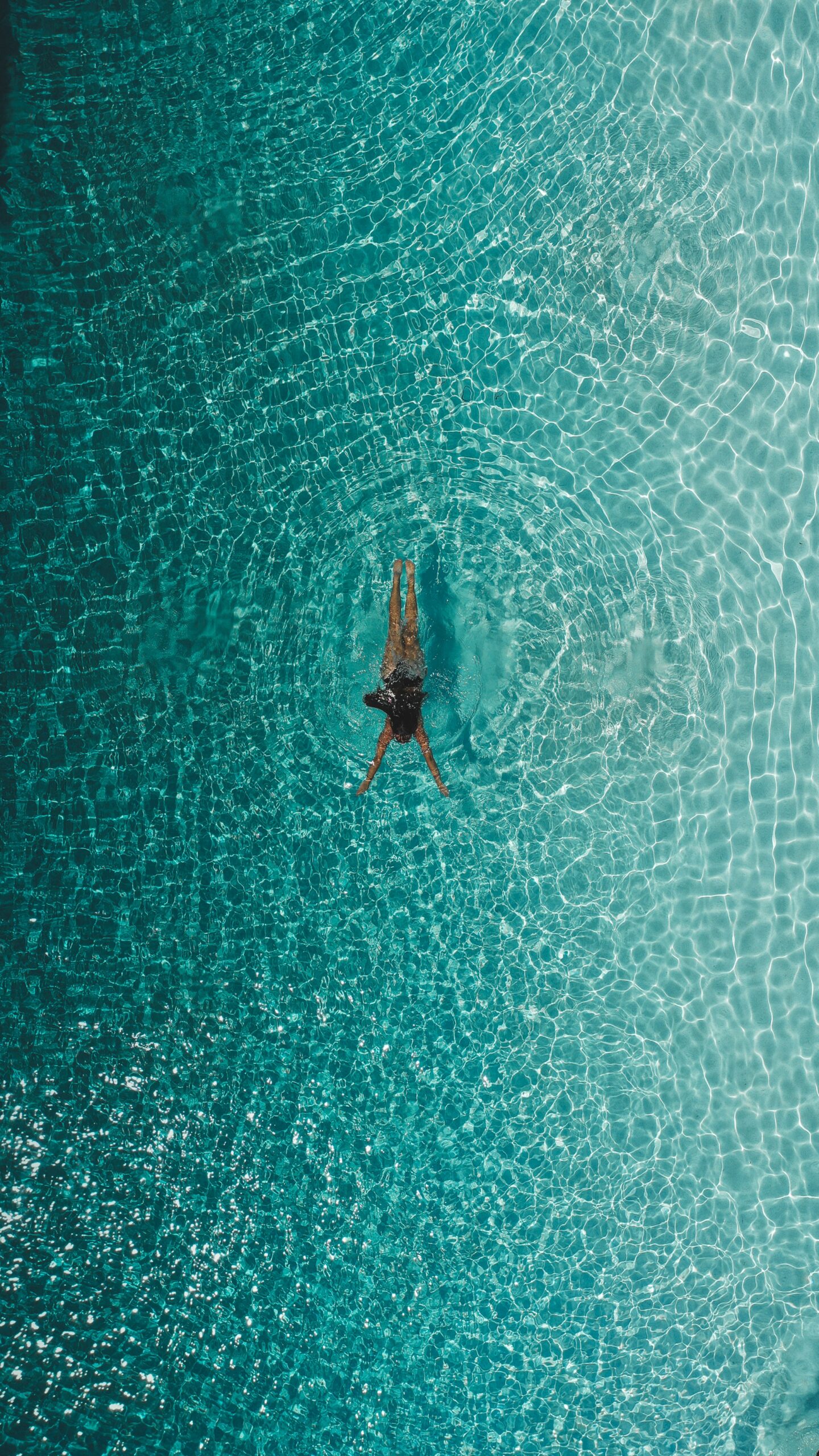 Femme nageant dans une eau cristalline vue du dessus, bras écartés