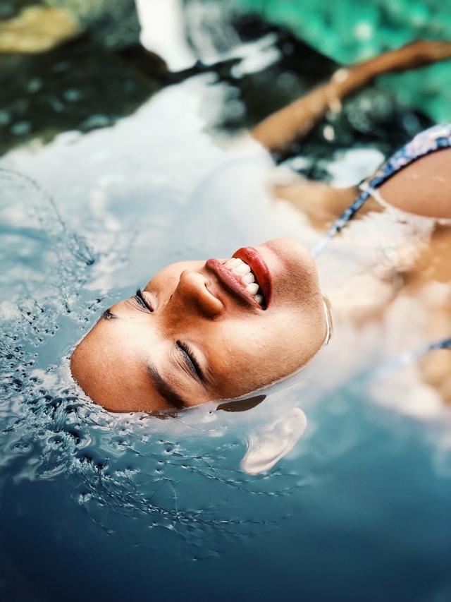 Femme souriante allongée dans l’eau chaude d’un spa, visage éclairé par la lumière