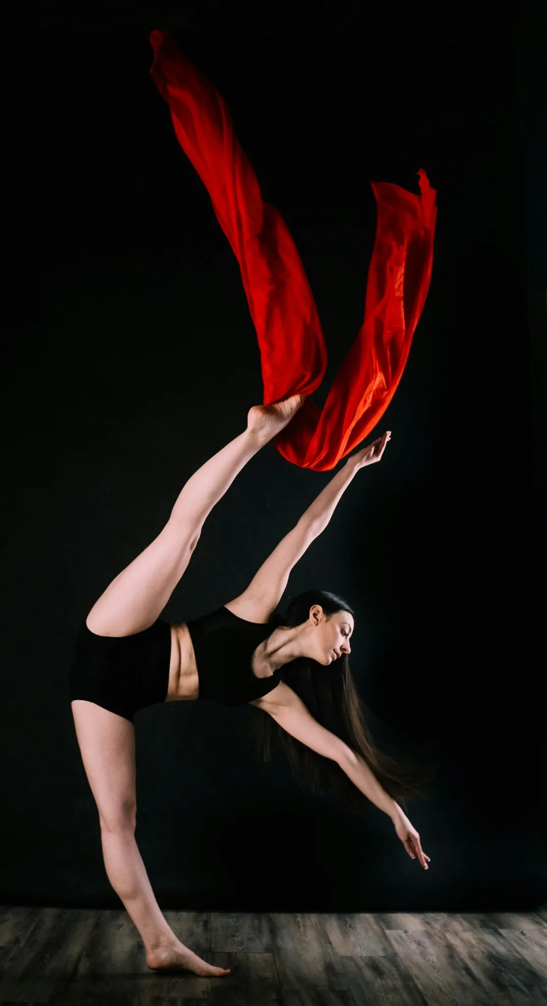 Femme exécutant une figure de danse aérienne avec tissu rouge, jambe tendue et posture élégante