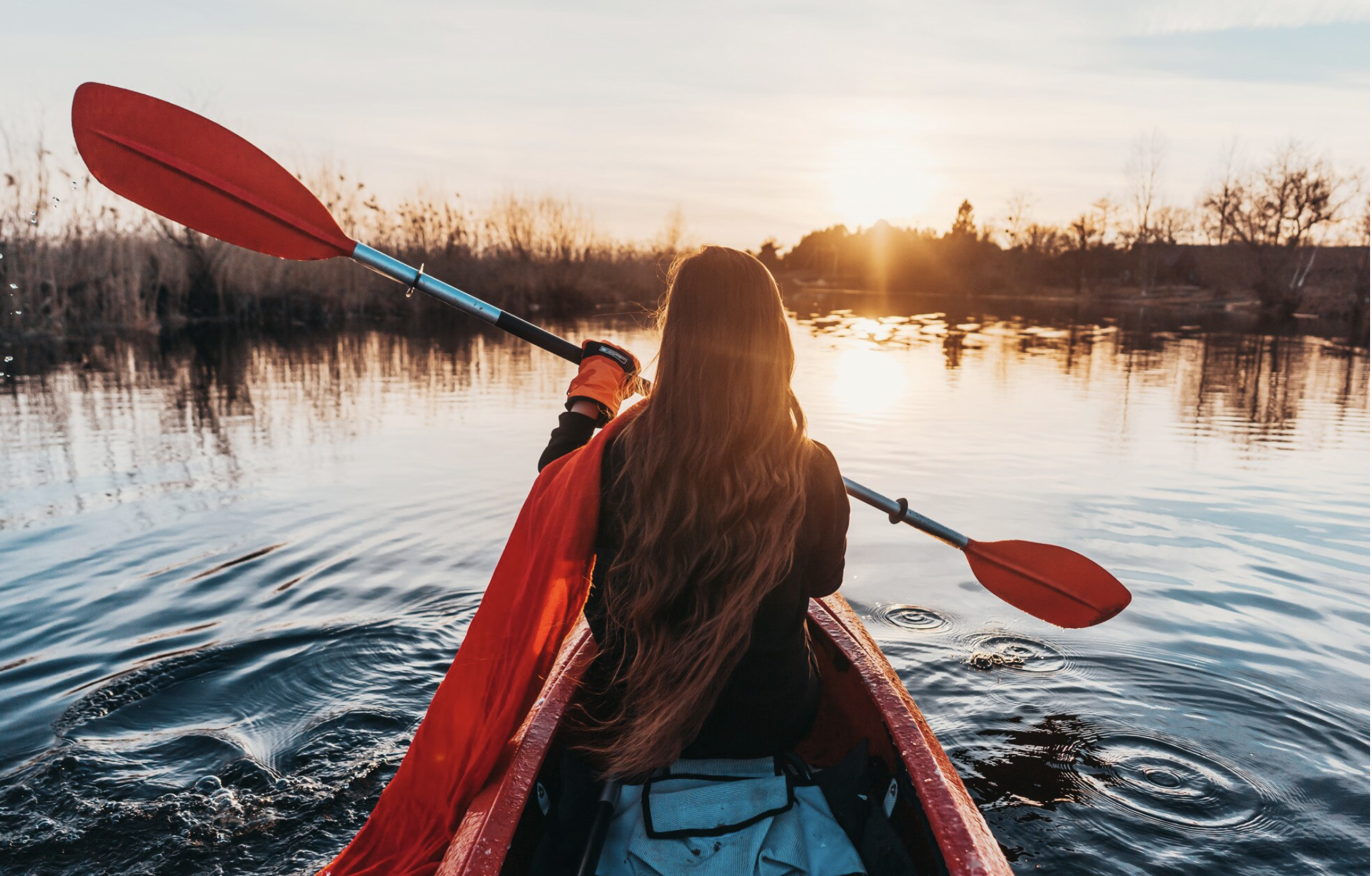 Femme seule assise dans un kayak, pagayant doucement sur le bassin d’Arcachon par temps ensoleillé, entourée d’eau et de nature.