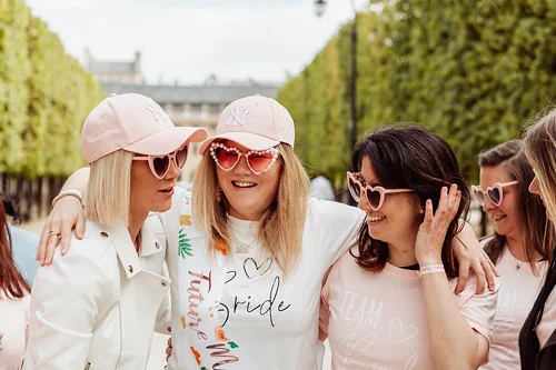 Future mariée souriante entourée de ses amies en t-shirts et lunettes roses lors d’un EVJF à Paris