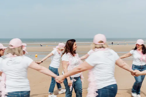 femmes en casquette rose et t shirt blanc formant une ronde sur la plage de cabourg pendant un evjf