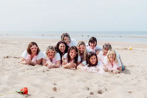groupe de femmes avec lunettes roses en forme de coeur allongees sur le sable lors d un evjf a cabourg