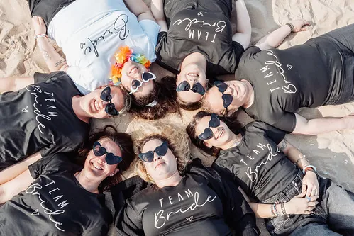 amies en t shirts team bride allongees en cercle sur le sable avec des lunettes coeur pendant un evjf a cabourg