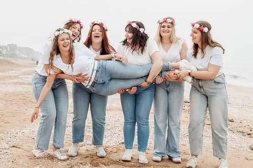 groupe de femmes en jean et t shirt blanc portant la mariee sur la plage de cabourg pendant un evjf