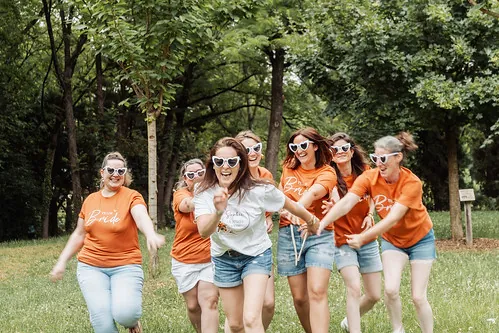 groupe de femmes en t shirt orange courant après la future mariee lors d un evjf en plein air