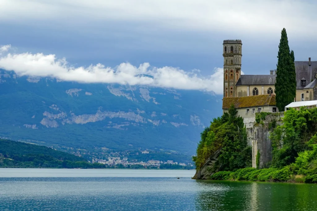 Abbaye de Hautecombe dominant le lac du Bourget avec les montagnes en arrière-plan sous un ciel nuageux.