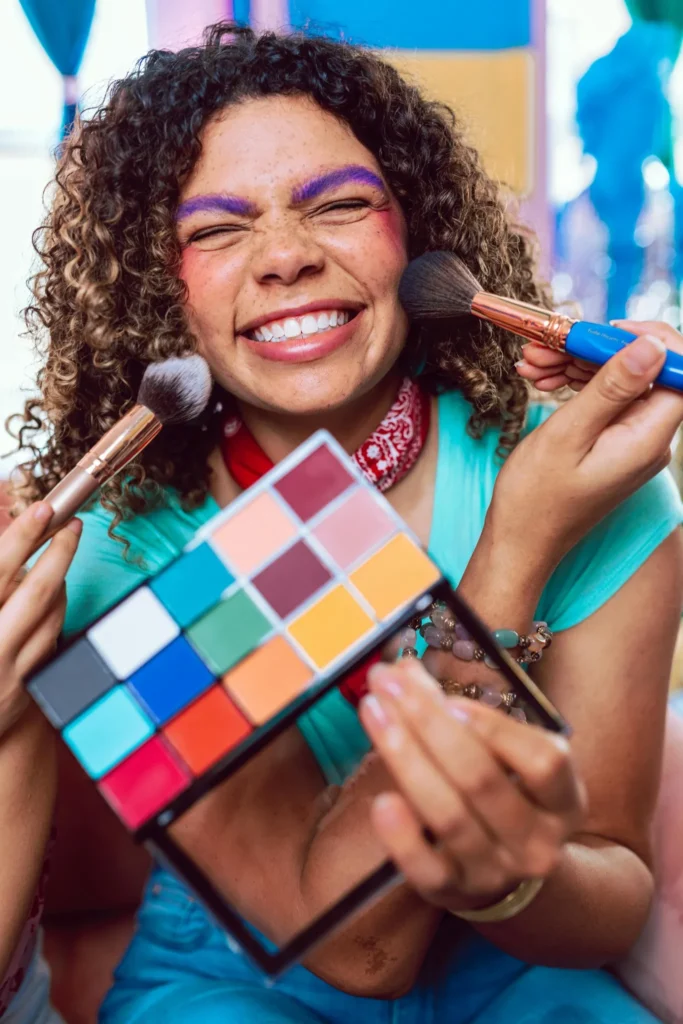 Femme souriante avec maquillage coloré et artistique, tenant une palette à Aix-en-Provence.