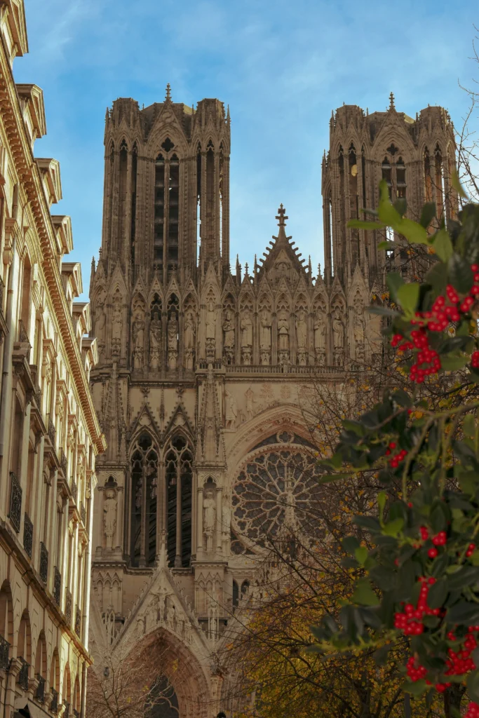 Vue hivernale de la majestueuse cathédrale Notre-Dame de Reims, entourée d’architecture classique et de végétation colorée, parfaite pour illustrer le charme historique de la ville.