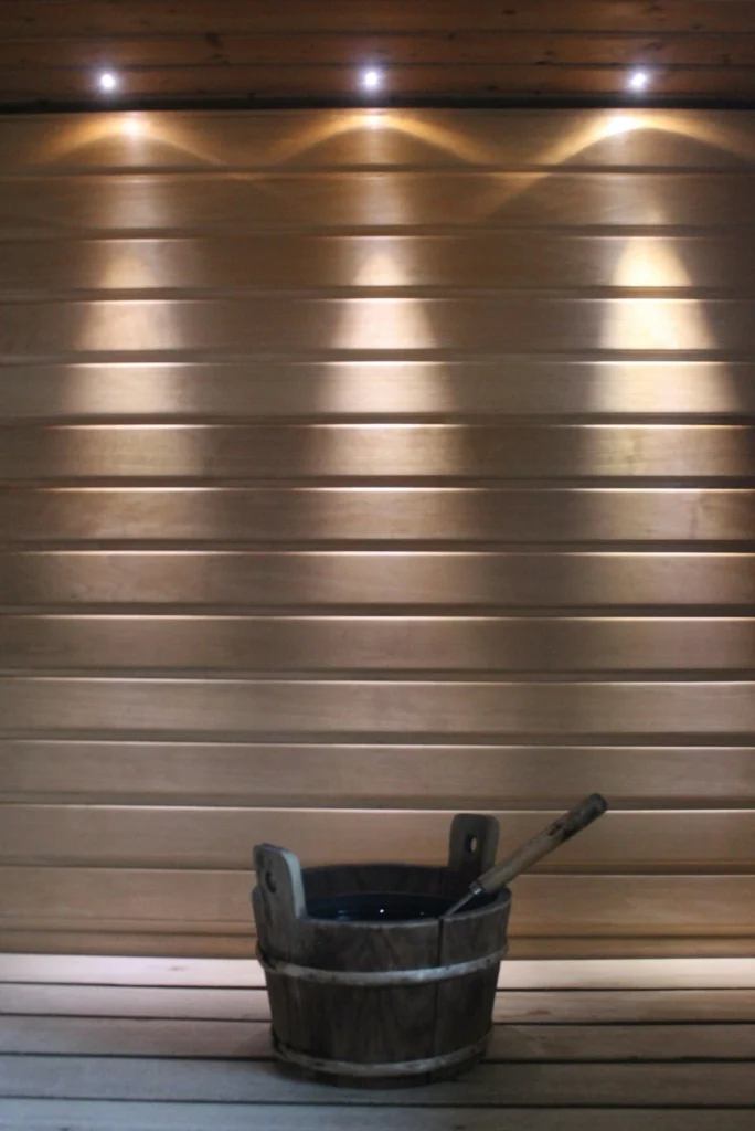 Seau en bois traditionnel posé au sol dans un sauna éclairé tamisé