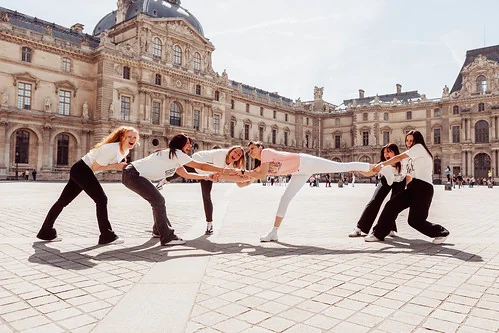 Amies souriantes posant de façon ludique devant le Louvre lors d’un shooting photo EVJF à Paris