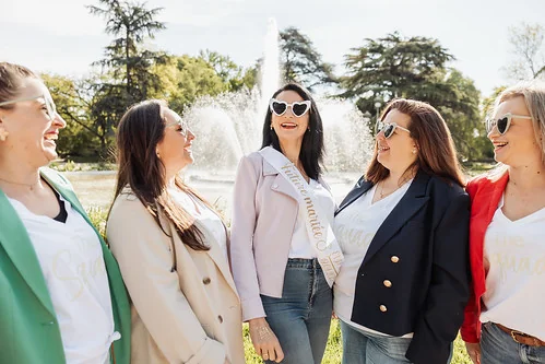 groupe de femmes souriantes en blazer coloré entourant la future mariee devant une fontaine lors d un shooting photo evjf a toulouse