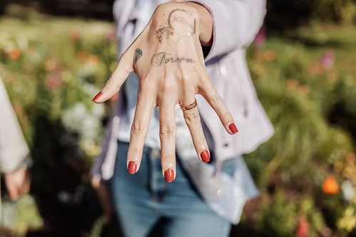 main d une femme avec manucure rouge montrant une bague et un tatouage