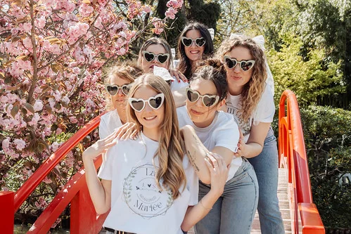 groupe de femmes souriantes en lunettes coeur posant ensemble lors d un shooting photo evjf a toulouse dans un parc fleuri