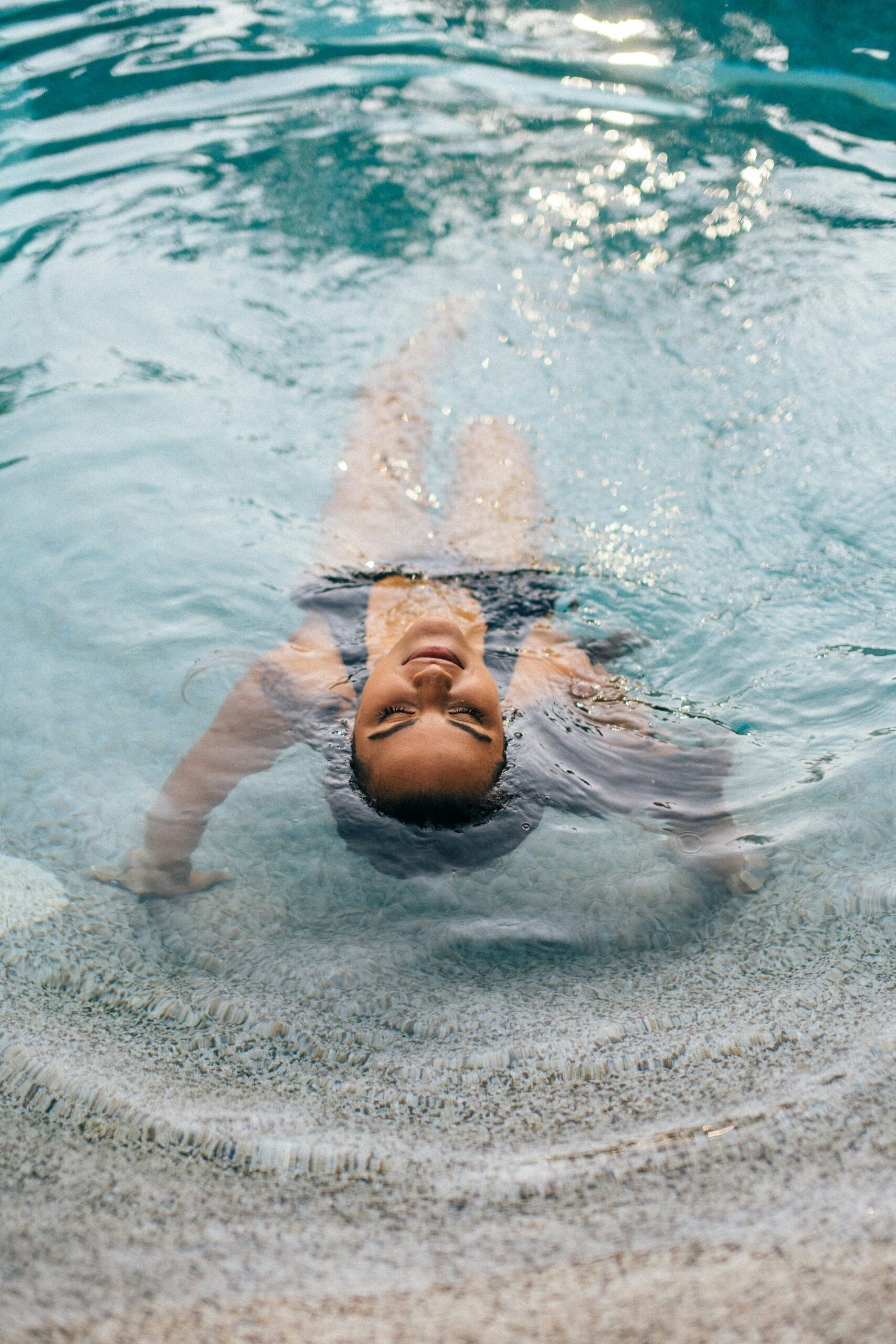 Femme détendue flottant sur le dos dans un bassin intérieur de spa, yeux fermés