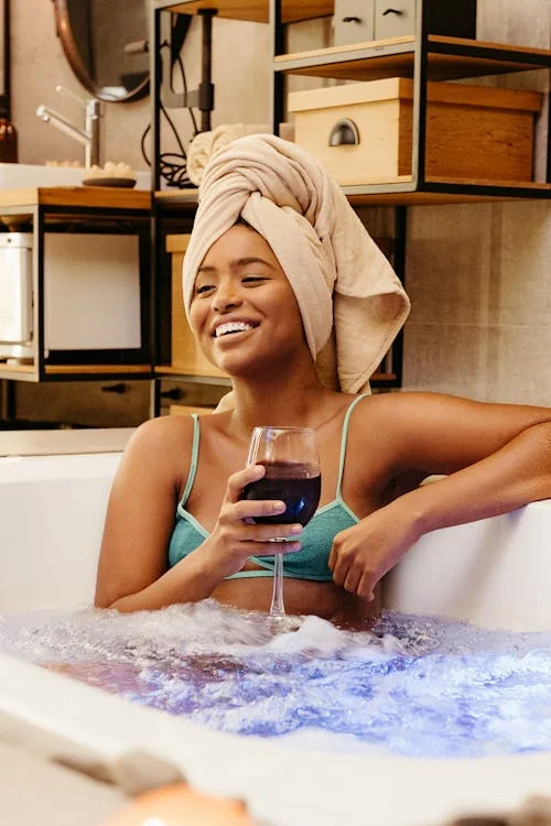 Femme souriante dans un bain à remous au spa de Deauville, serviette sur la tête et verre de vin rouge à la main