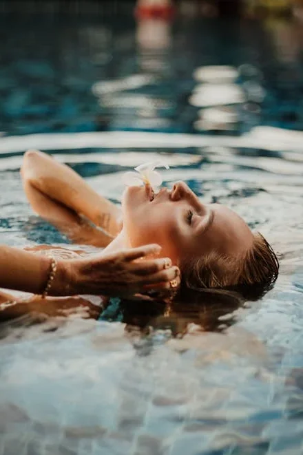 Femme se relaxant dans une piscine de spa à Lille, tenant une fleur blanche près du visage, ambiance détente et bien-être