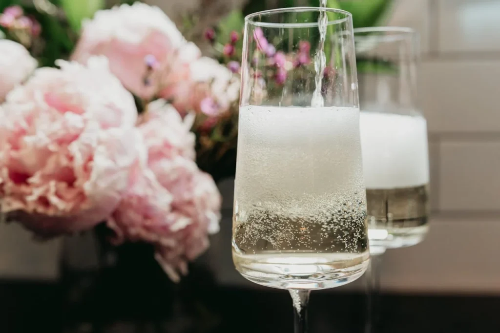 Verres de champagne pétillant avec bouquet de fleurs roses en arrière-plan pour un brunch EVJF à Paris