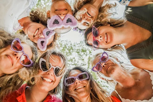 amies en cercle regardant l’objectif, lunettes fantaisie violettes en extérieur