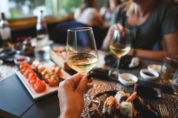 verre de vin blanc levé lors d’un repas convivial avec sushis représentant des activités culturelles pour evjf à toulouse de nuit