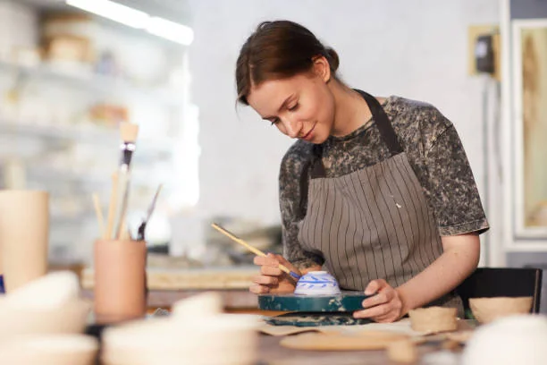 Atelier céramique dans un café céramique EVJF à Strasbourg, jeune femme décorant un bol en argile avec un pinceau