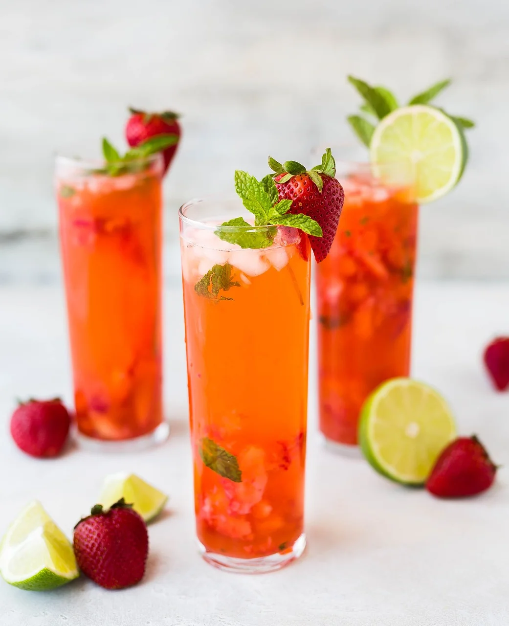 Cocktail rouge aux fraises et à la menthe garni de citron vert et de fruits frais