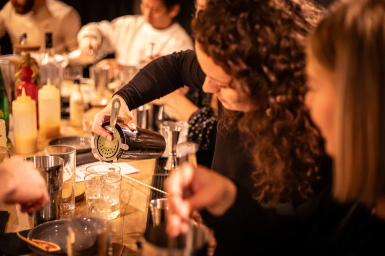 Participant concentré versant un cocktail avec un shaker dans un verre rempli de glaçons