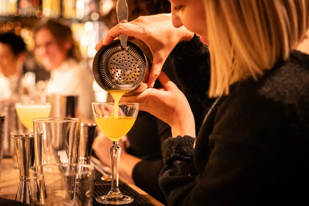 Préparation d’un cocktail jaune versé dans un verre à pied lors d’un atelier mixologie