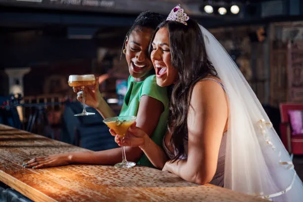 Future mariée portant un voile et une couronne partageant un cocktail avec une amie dans un bar lors d un evjf à Strasbourg