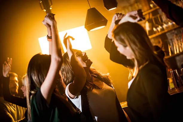 Jeunes femmes dansant et levant les bras dans un bar à Strasbourg lors d un evjf dans une ambiance festive et conviviale