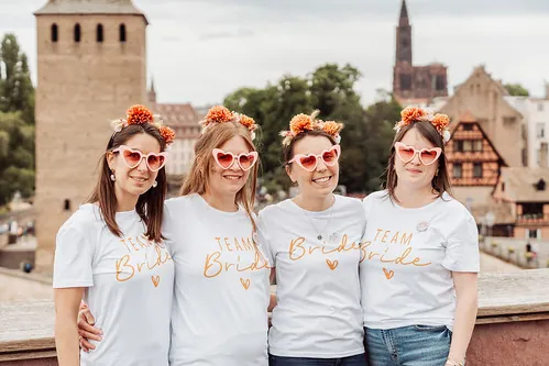 Quatre amies en t shirt team bride posant avec des lunettes coeur à Strasbourg lors d un evjf avec vue sur la ville