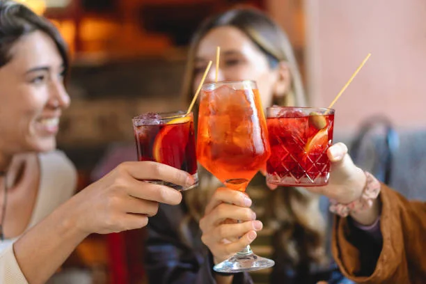 trois copines trinquent avec des cocktails colores dans un bar convivial de toulouse parfait pour un evjf festif
