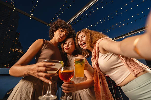 trois amies prennent un selfie en terrasse rooftop de nuit a toulouse avec des cocktails ambiance ideale pour un evjf