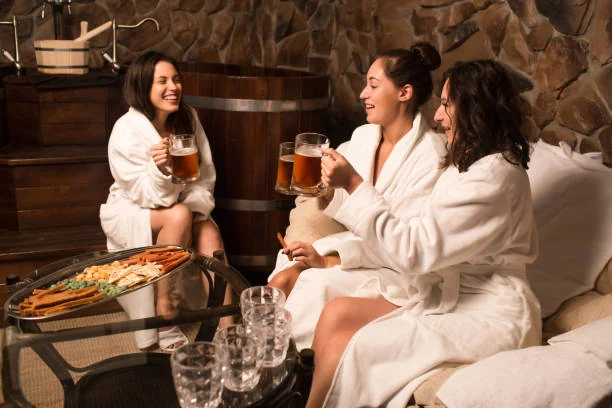 Beer spa EVJF à Strasbourg, trois amies en peignoir trinquent avec des chopes de bière dans un espace bien-être convivial