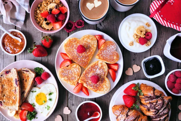 Assortiment de pancakes en forme de cœur, croissants, fruits frais et cafés décorés pour un brunch EVJF à Nantes.