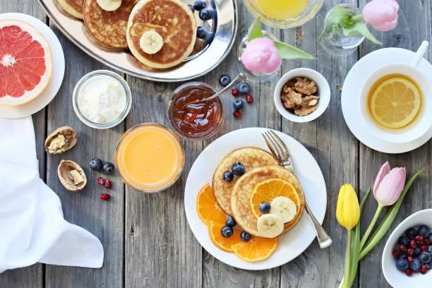 Assiette de pancakes avec fruits frais, jus et café sur une table en bois lors d’un brunch EVJF à Rouen