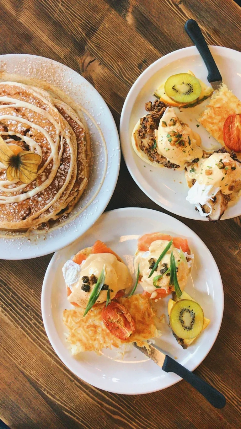 Assiettes de pancakes et œufs bénédicte avec fruits frais et kiwi sur table en bois