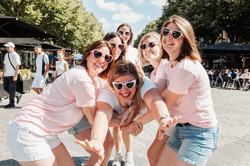 groupe de femmes en t shirts roses et lunettes en coeur posant ensemble dans la rue lors d une chasse au tresor evjf a reims