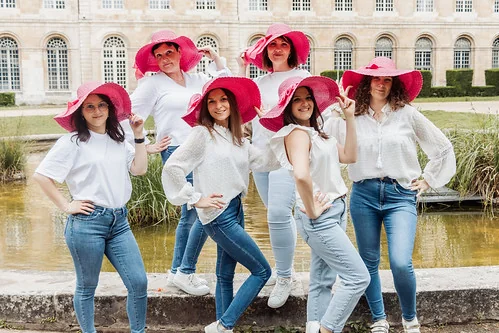 Groupe de femmes souriantes en chapeau rose posant lors d’un clip vidéo EVJF à Rouen devant un bâtiment historique