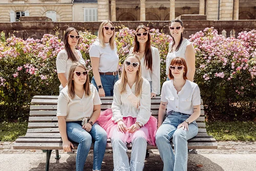 clip vidéo evjf à bordeaux avec groupe de femmes portant des lunettes en forme de cœur assises sur un banc devant des fleurs